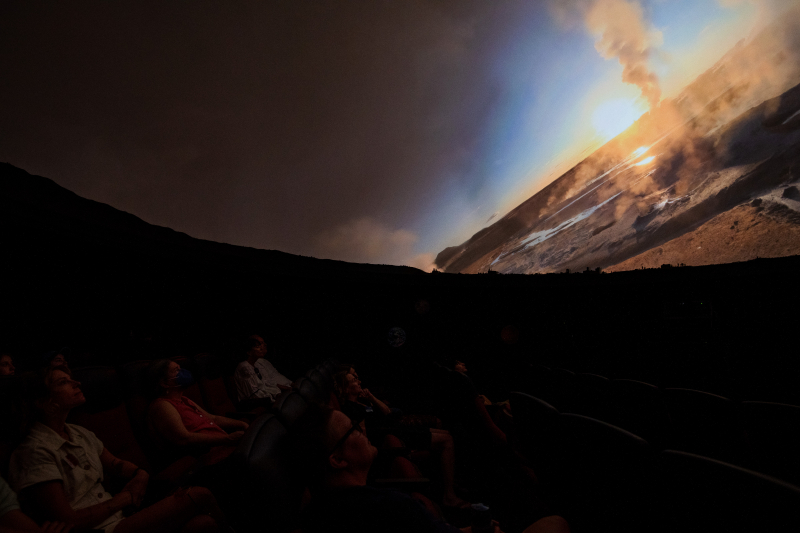 people in a dark theater watching a mysterious landscape unfold overhead on the planetarium dome