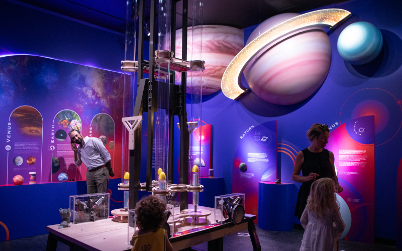 guests exploring an astronomy exhibit under giant models of the planets