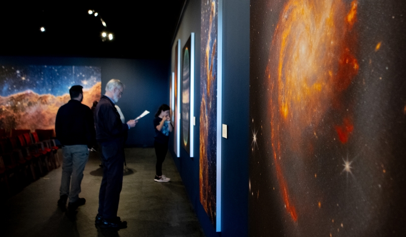 Giant cosmic images of swirling galaxies and fuzzy nebulae in a darkened gallery space with a few guests