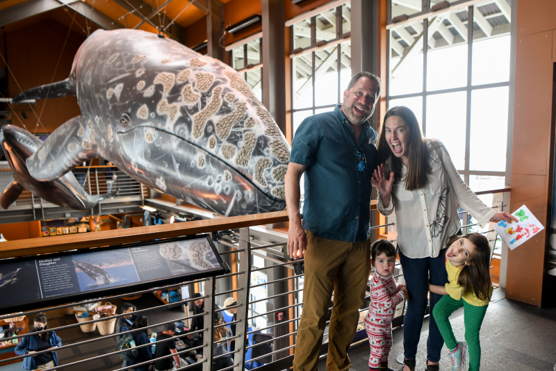 a happy family posing in front of a giant whale replica at the Sea Center