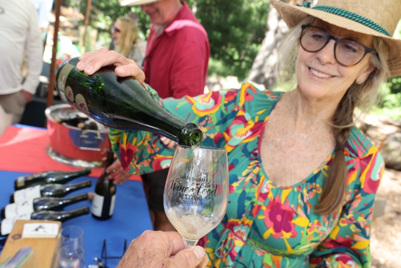 Smiling woman pours white wine into the photographer's glass in a wooded landscape