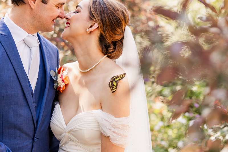 romantic bride and groom in the butterfly pavilion with a Malachite butterfly on bride's bare shoulder